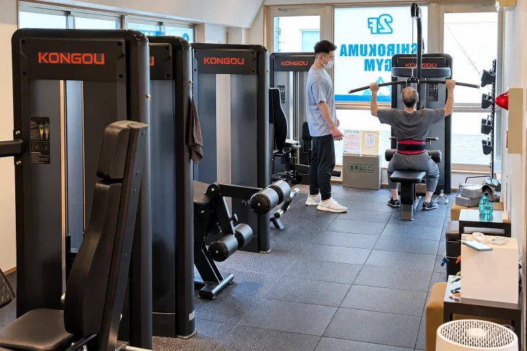 会員がマシンで運動し、そばでトレーナーが見守るジムの様子
